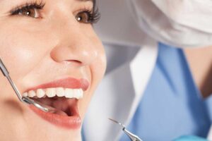 A person holding a whitening strip and about to apply it to their upper teeth in front of a bathroom mirror.