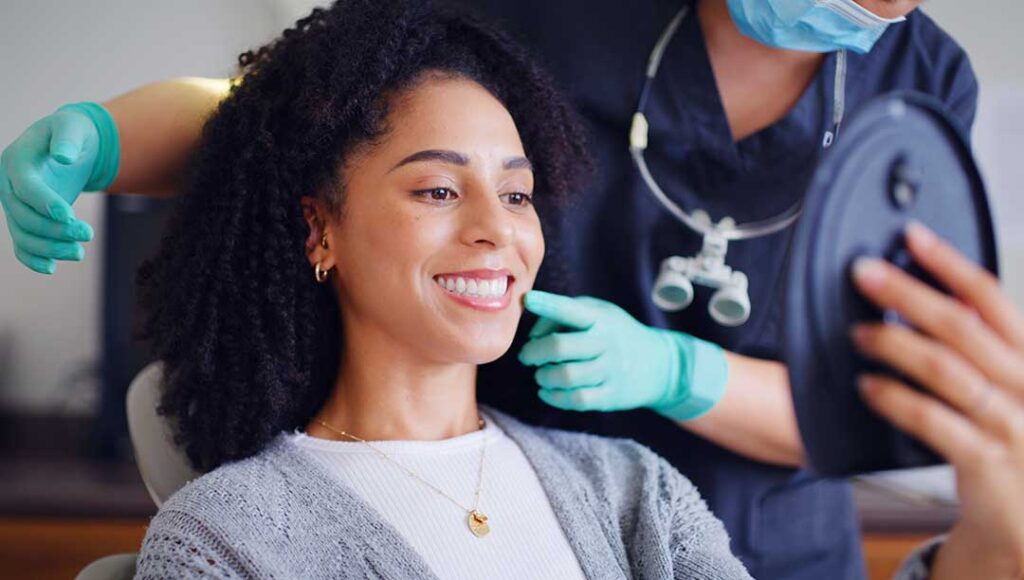 Dental professional examining a patient’s gum line with a mirror and dental instruments in a bright treatment room.