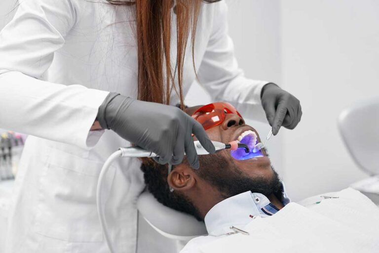 A dentist discussing smile options with a patient using a tooth shade guide in a bright dental office.